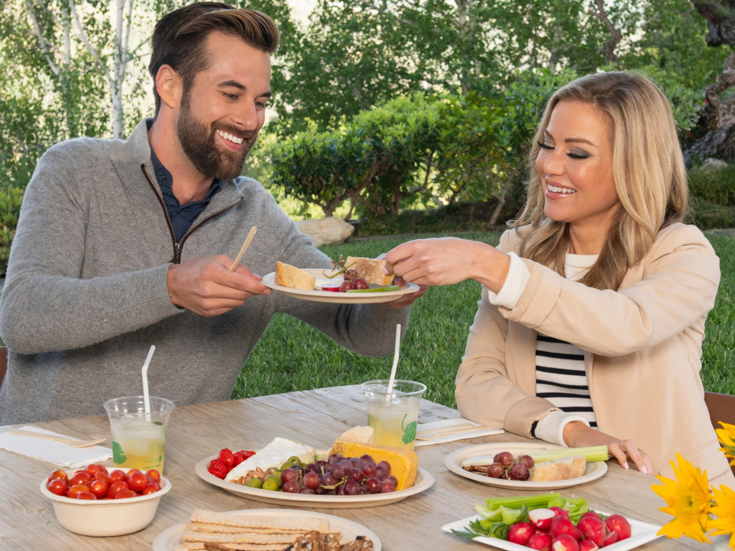Man and woman enjoying a meal outdoors with drinks and snacks on a table.